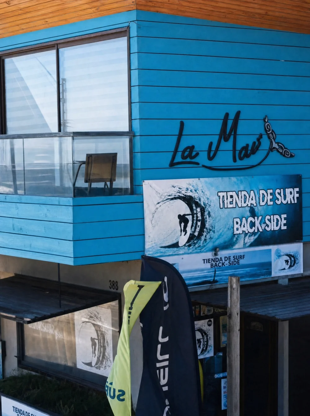 Fachada real de Backside: madera azul, ventanales y letrero